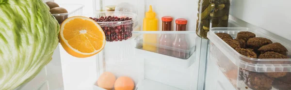 Foto panorámica de frutas frescas con croquetas de col y salsas en nevera con puerta abierta aislada en blanco - foto de stock