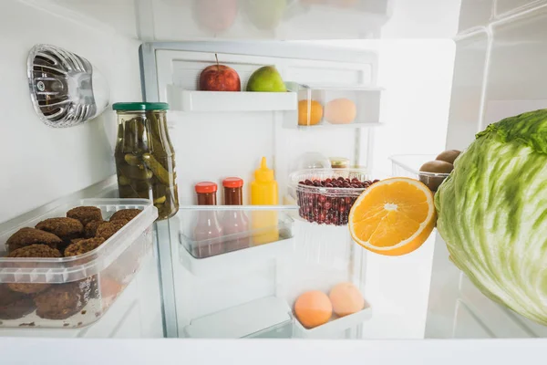 Costolette con frutta matura e cavolo in frigorifero con porta aperta isolata su bianco — Foto stock