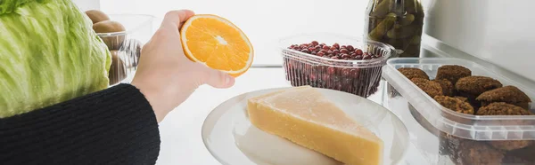 Abgeschnittene Ansicht einer Frau, die Orangenscheiben aus dem Kühlschrank nimmt, mit Lebensmitteln isoliert auf weißem Hintergrund, Panoramaaufnahme — Stockfoto