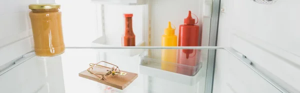 Панорамный снимок мышеловки в холодильнике с соусами и открытой дверью, изолированной на белом — стоковое фото
