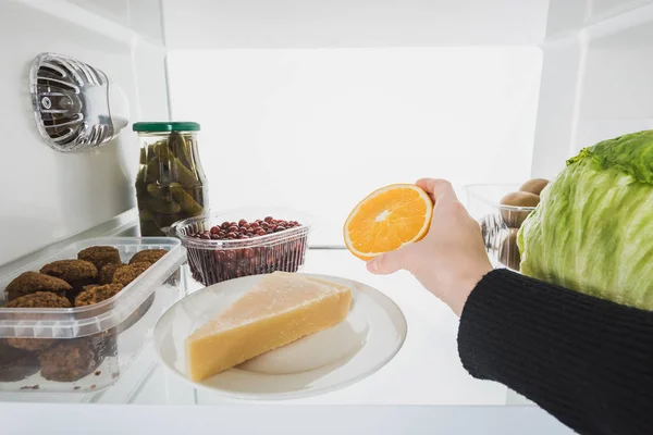Vista recortada de la mujer tomando rebanada de naranja de la nevera con alimentos aislados en blanco - foto de stock