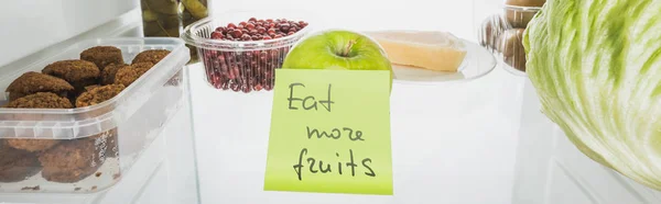 Panoramic shot of card with eat more fruits lettering in fridge with food isolated on white — Stock Photo