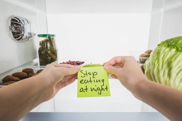 Vista recortada da mulher cartão de retenção com parar de comer à noite lettering com alimentos na geladeira isolado no branco — Fotografia de Stock