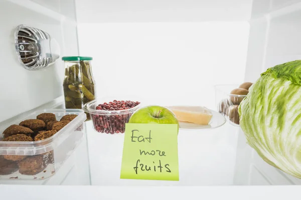 Cartão com comer mais frutas lettering na prateleira do refrigerador com alimentos isolados em branco — Fotografia de Stock