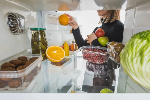 Vista recortada de la mujer que toma frutas maduras del refrigerador con alimentos aislados en blanco - foto de stock