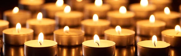 Selective focus of burning candles glowing in darkness, panoramic shot — Stock Photo