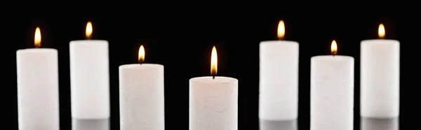 Selektiver Fokus brennender weißer Kerzen, die isoliert auf schwarzer, panoramischer Aufnahme glühen — Stockfoto
