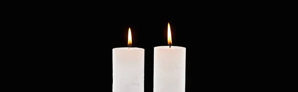 Zwei brennende weiße Kerzen, die isoliert auf schwarzer, panoramischer Aufnahme glühen — Stockfoto