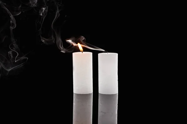 Velas blancas ardientes y extinguidas con humo sobre fondo negro - foto de stock