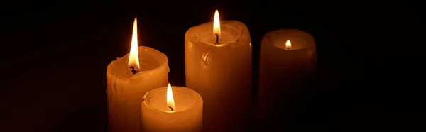 Brennende Kerzen, die in der Dunkelheit auf schwarzem Hintergrund glühen, Panoramaaufnahme — Stockfoto