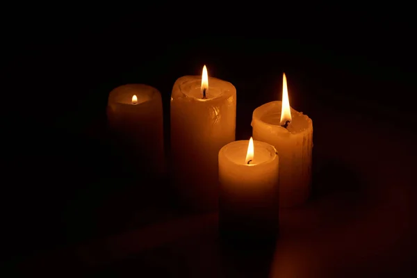 Brennende Kerzen, die in der Dunkelheit auf schwarzem Hintergrund glühen — Stockfoto