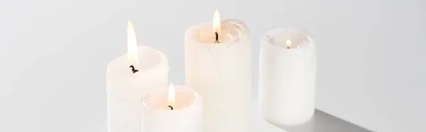 Burning candles glowing on white background with shadow, panoramic shot — Stock Photo