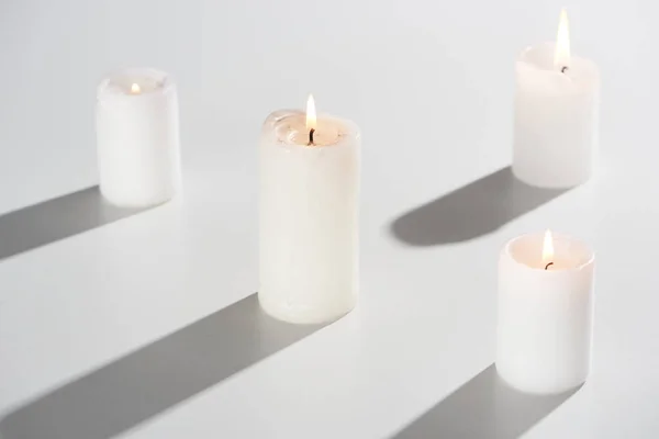 Velas ardientes que brillan sobre fondo blanco con sombra - foto de stock