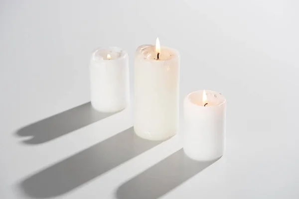 Velas ardientes que brillan sobre fondo blanco con sombra - foto de stock