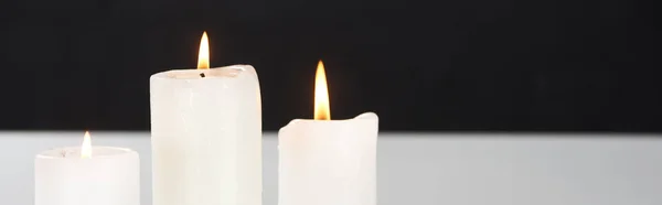 Burning white candles on white surface glowing isolated on black, panoramic shot — Stock Photo