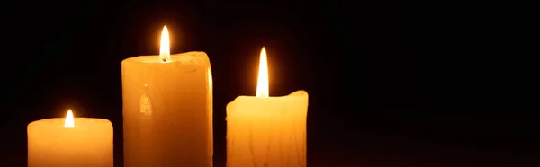 Burning candles glowing in dark isolated on black, panoramic shot — Stock Photo