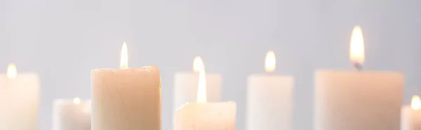 Selective focus of burning white candles glowing isolated on grey, panoramic shot — Stock Photo