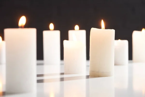 Selective focus of burning white candles on white surface glowing isolated on black — Stock Photo