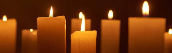 Selective focus of burning candles glowing in dark, panoramic shot — Stock Photo