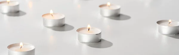 Selective focus of burning candles glowing on white surface, panoramic shot — Stock Photo
