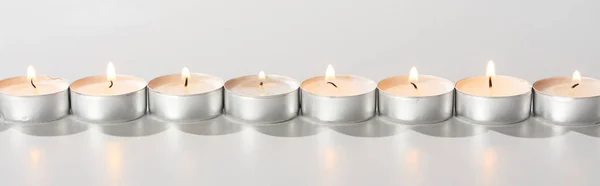 Velas ardientes brillando en línea sobre fondo blanco, plano panorámico - foto de stock