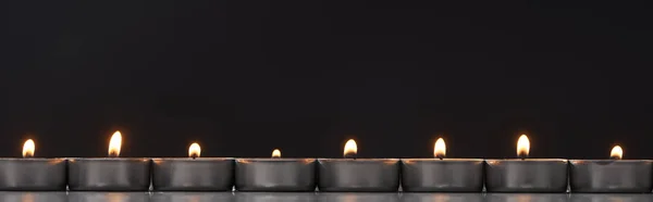 Burning candles arranged in line glowing isolated on black, panoramic shot — Stock Photo