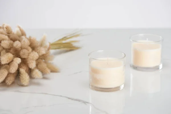 Selective focus of fluffy bunny tail grass and white candles in glass on marble white surface — Stock Photo