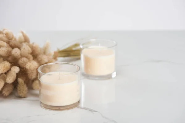 Enfoque selectivo de esponjoso conejito cola hierba y velas blancas en vidrio sobre mármol superficie blanca - foto de stock