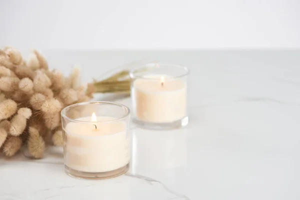 Selective focus of fluffy bunny tail grass and burning white candles in glass glowing on marble white surface — Stock Photo