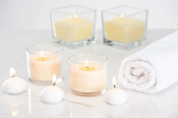 Burning white candles in glass and rolled towel on marble white surface — Stock Photo