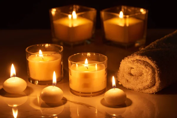 Selective focus of burning candles in glass glowing in dark near rolled towel on marble surface — Stock Photo