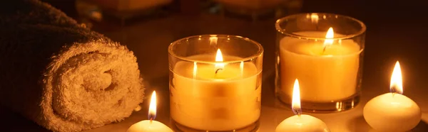 Горящие свечи в стекле, светящиеся в темноте возле скатного полотенца на мраморной поверхности, панорамный снимок — стоковое фото