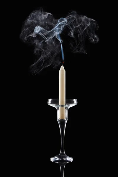 Extinct white candle in glass candlestick with smoke on black background — Stock Photo