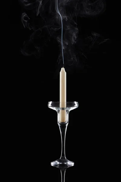 Extinct white candle in glass candlestick with smoke on black background — Stock Photo