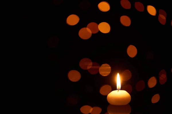 Brennende Kerze, die im Dunkeln mit Bokeh-Lichtern auf dem Hintergrund glüht — Stockfoto