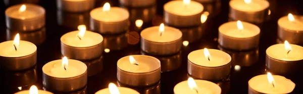 Selektiver Fokus brennender Kerzen, die in der Dunkelheit glühen, Panoramaaufnahme — Stockfoto