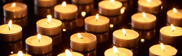 Selective focus of burning candles glowing in darkness, panoramic shot — Stock Photo