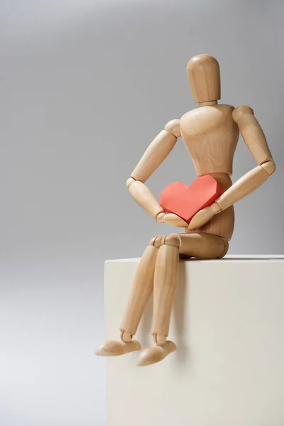 Деревянная кукла с бумагой в форме сердца на кубе на сером фоне — стоковое фото