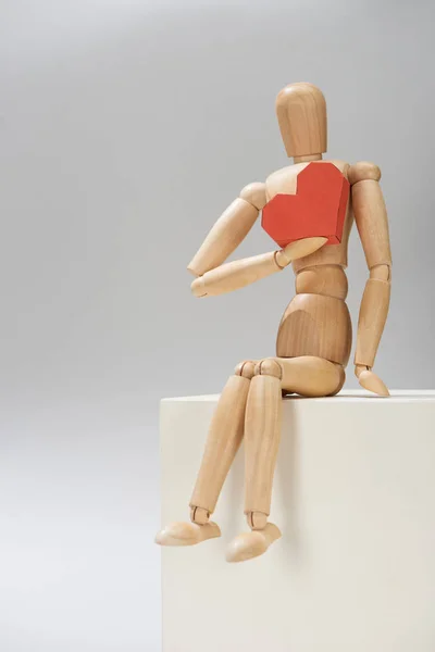 Marioneta de madera con corazón de papel rojo en pie sobre fondo gris - foto de stock