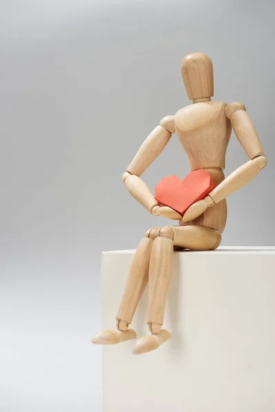 Muñeca de madera con papel rojo en forma de corazón en pie sobre fondo gris - foto de stock