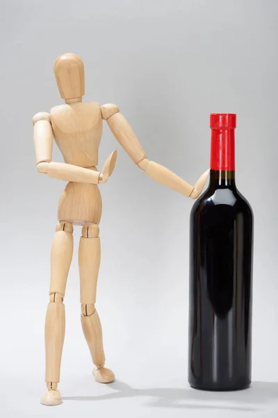 Wooden doll with bottle of red wine on grey background — Stock Photo