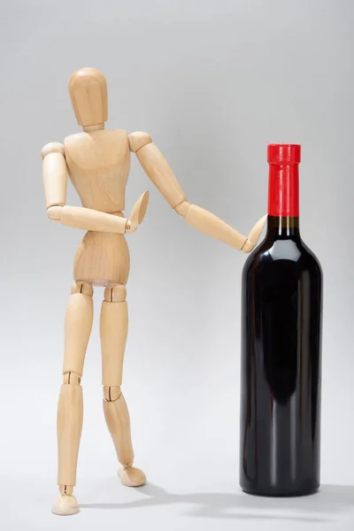 Boneca de madeira com garrafa de vinho tinto sobre fundo cinza — Fotografia de Stock