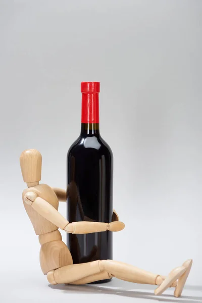 Marioneta de madera junto a una botella de vino tinto sobre fondo gris - foto de stock