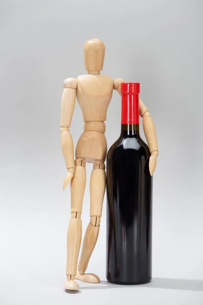 Muñeca de madera y botella de vino tinto sobre fondo gris - foto de stock