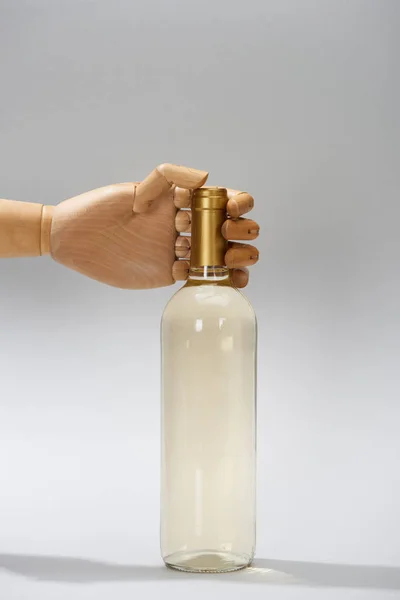 Hand einer Holzpuppe mit Flasche Weißwein auf grauem Hintergrund — Stockfoto