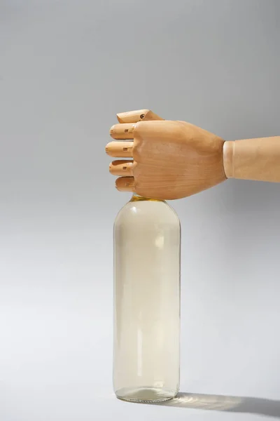 Mano de madera de maniquí con botella de vino sobre fondo gris - foto de stock