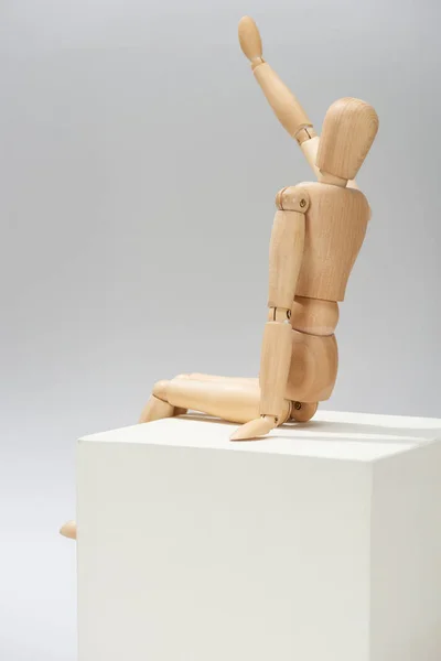 Marioneta de madera con la mano extendida sobre cubo blanco sobre fondo gris - foto de stock