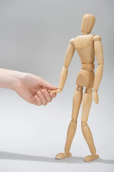 Cropped view of woman holding hand of wooden doll on grey background — Stock Photo