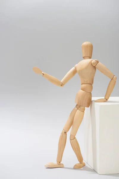 Mannequin en bois par stand blanc pointant avec la main sur fond gris — Photo de stock