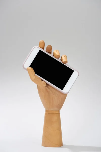 Mão de madeira de boneca com smartphone com tela em branco no fundo cinza — Fotografia de Stock